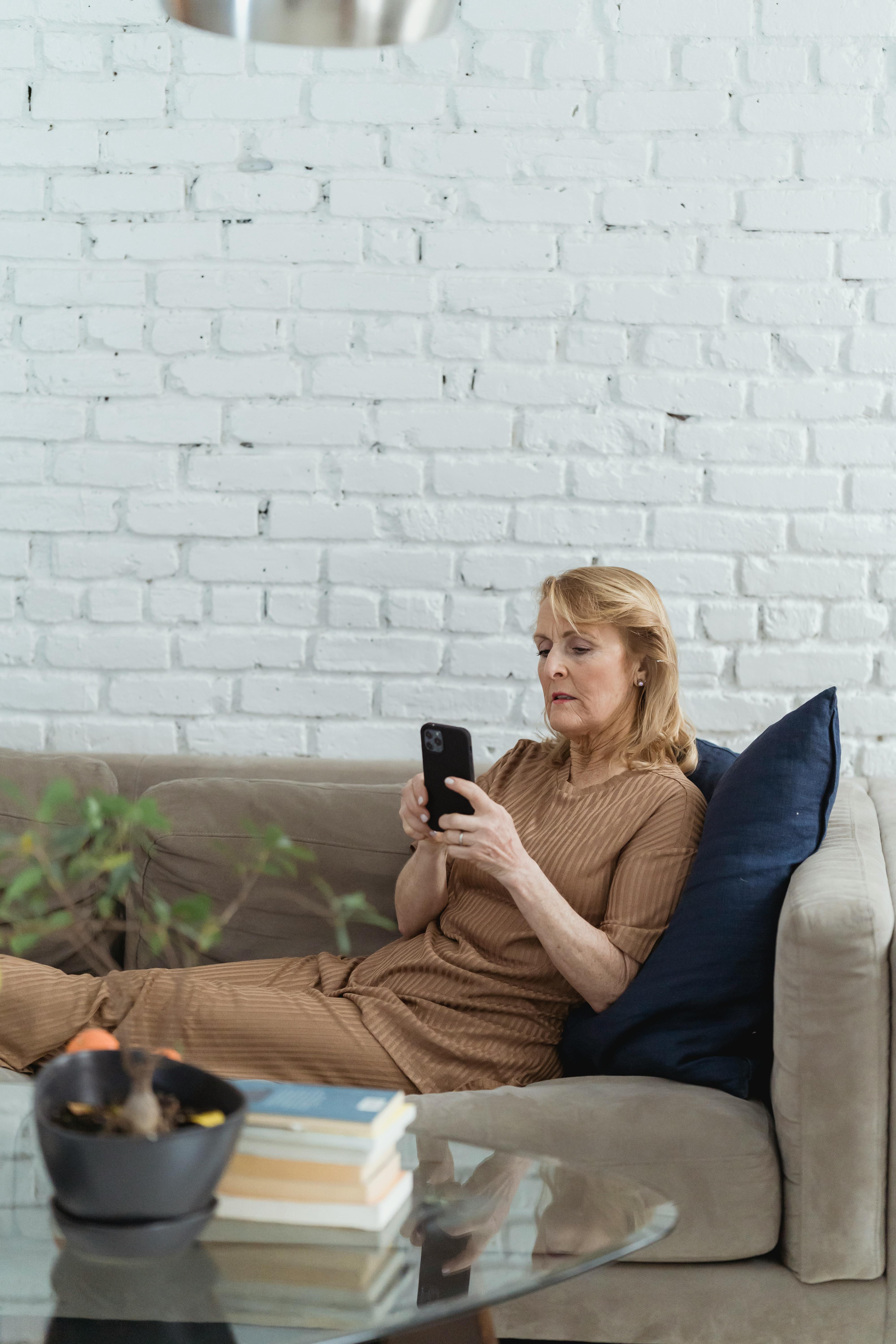 senior woman text messaging on smartphone on sofa at home