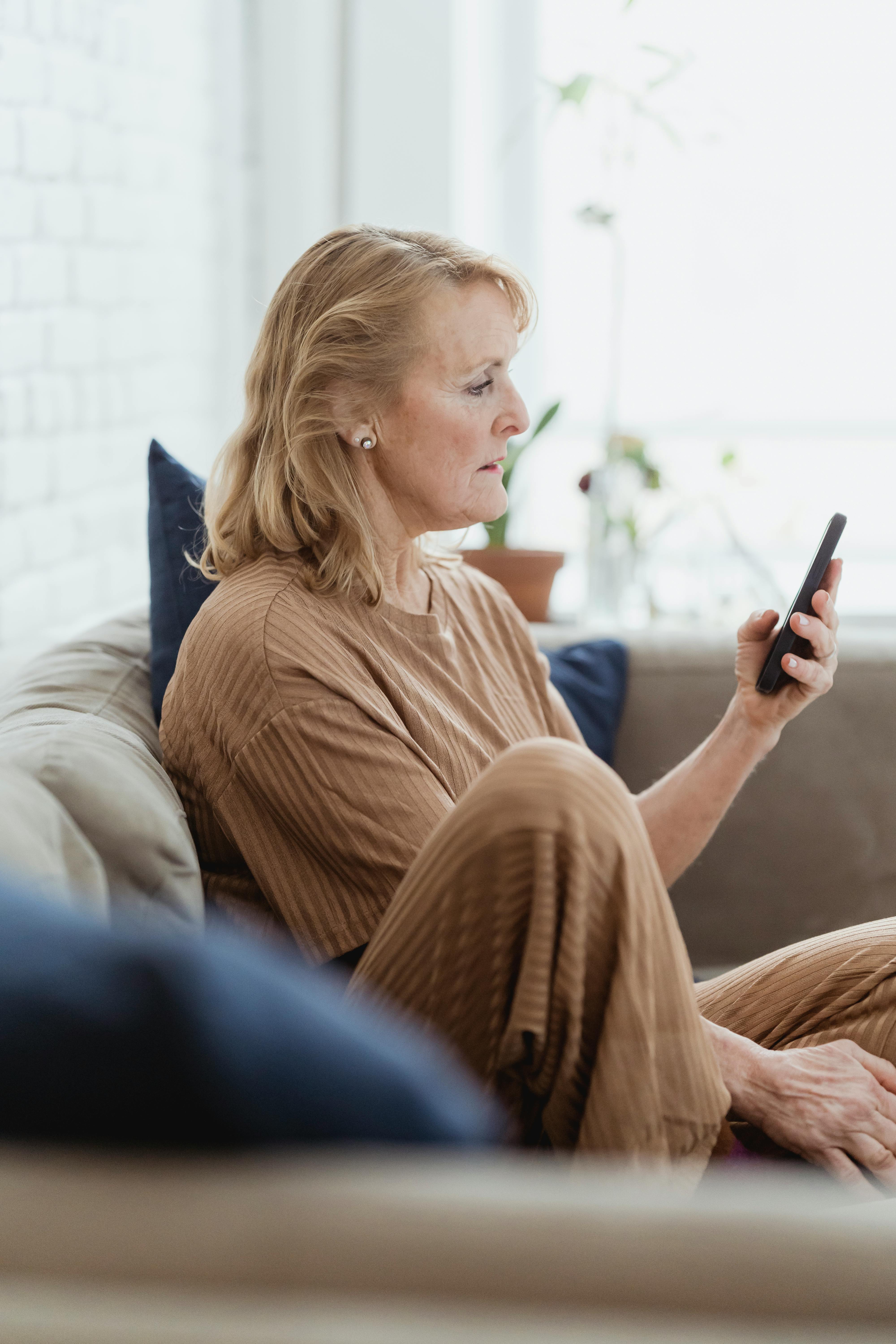 senior woman chatting on smartphone on sofa in house