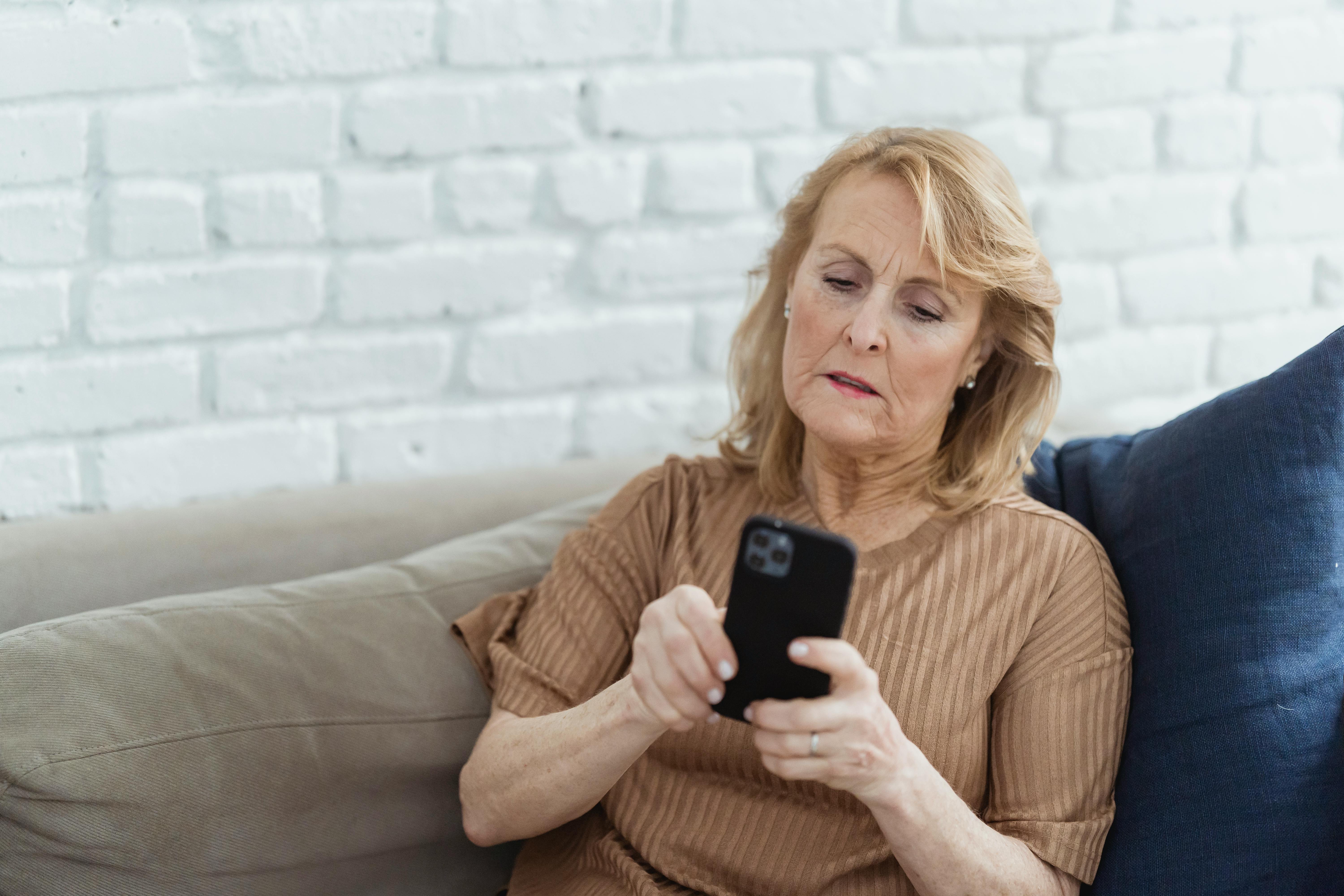 elderly woman chatting on smartphone on couch in house