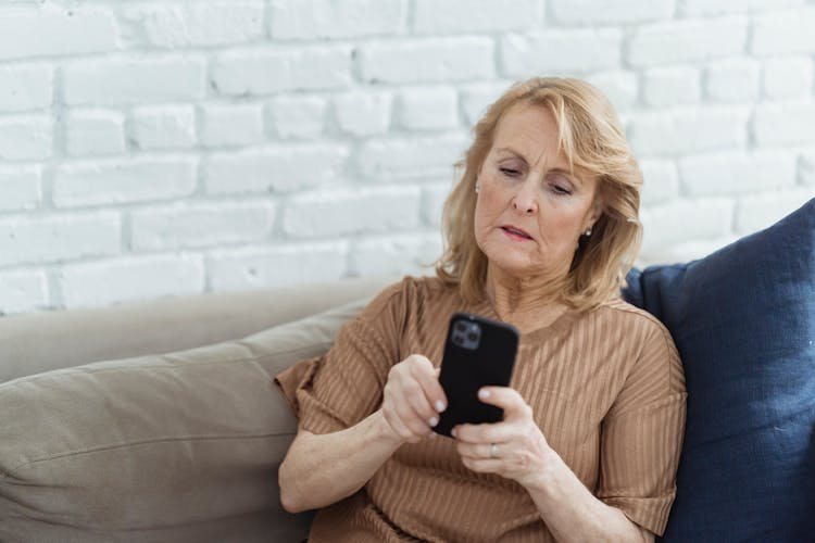 Elderly Woman Chatting On Smartphone On Couch In House