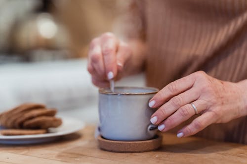 Free Crop unrecognizable female preparing hot beverage in mug at desk with tasty biscuits in house Stock Photo