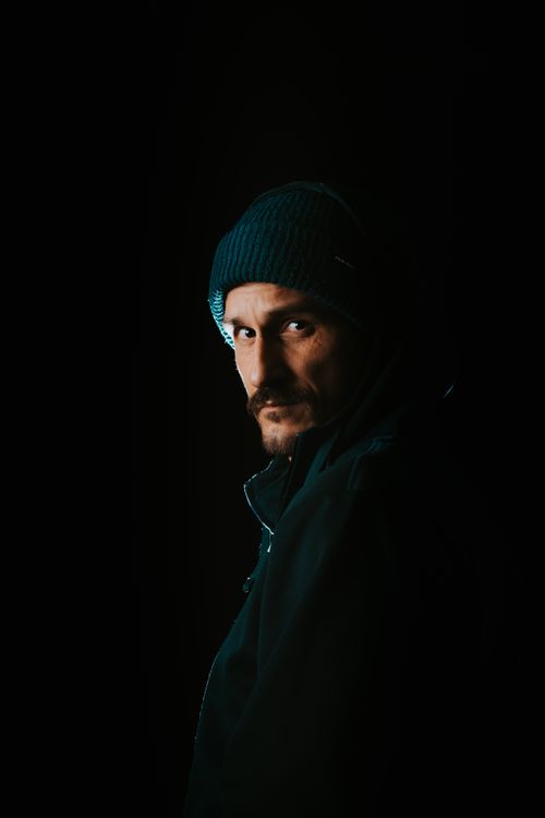 Free Dark and moody portrait of a man wearing a beanie and black jacket against a black background. Stock Photo