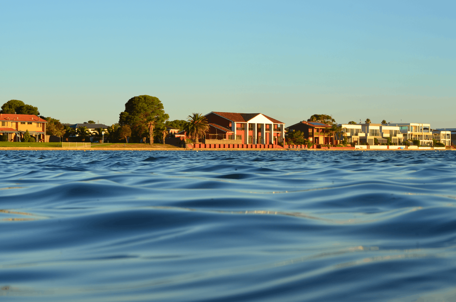 Stunning lakefront homes in West Lakes, Australia, with calm water and a clear blue sky.