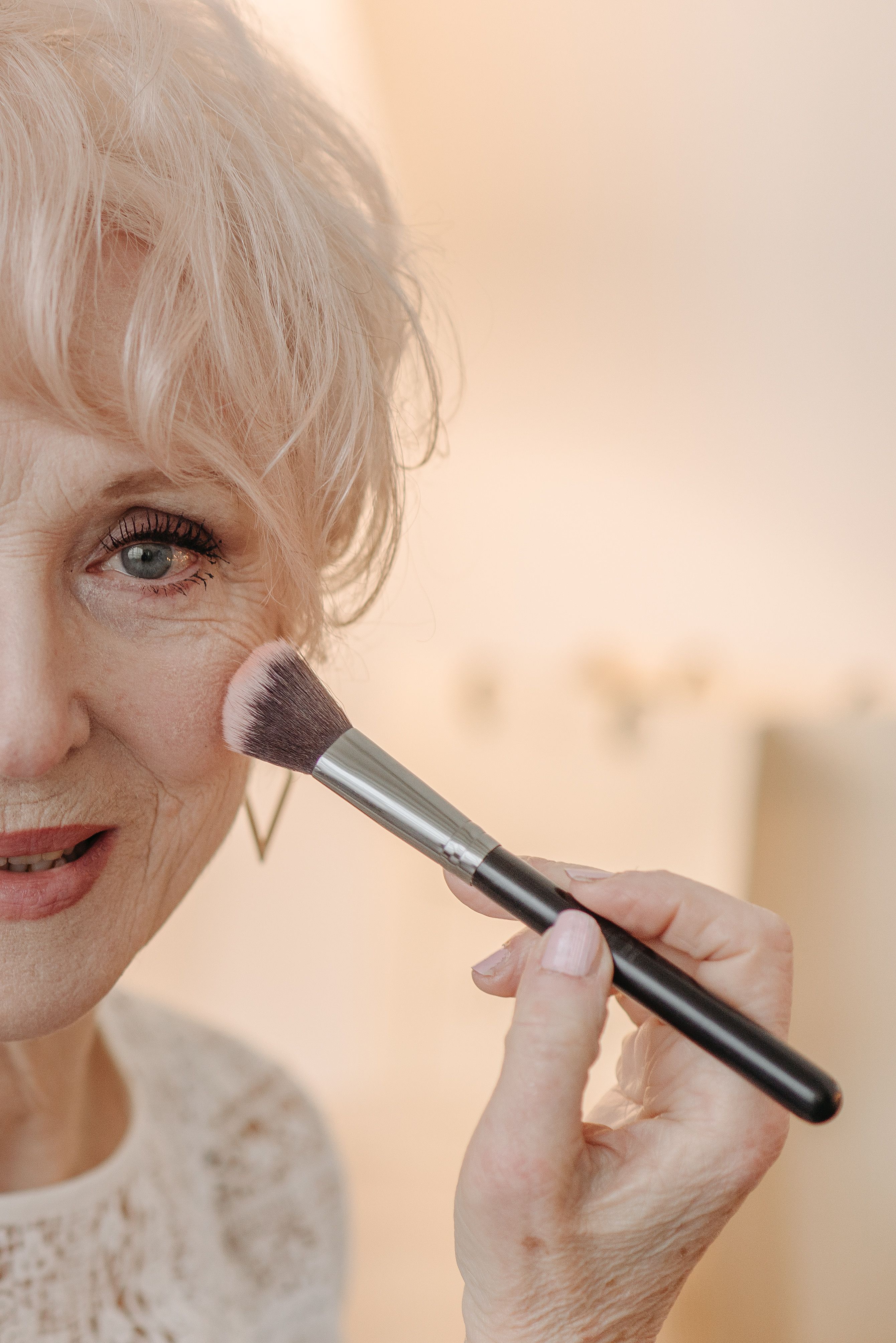 Senior woman using a makeup brush to apply blush, highlighting beauty at any age.