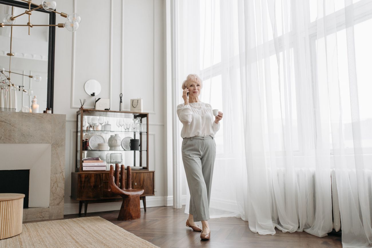 A woman walking through her home with a cup of tea while talking on the phone