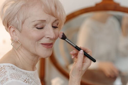 An Elderly Woman Applying Blush On Makeup