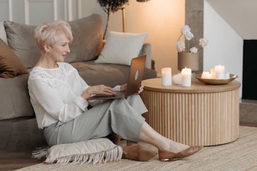 Senior woman enjoying working remotely at home with laptop and candles for a cozy ambiance.