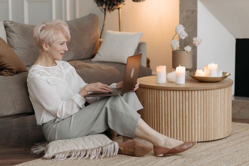 Free Senior woman enjoying working remotely at home with laptop and candles for a cozy ambiance. Stock Photo