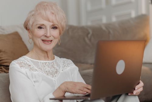 Free Smiling senior woman with blonde hair using a laptop in a cozy indoor setting. Stock Photo