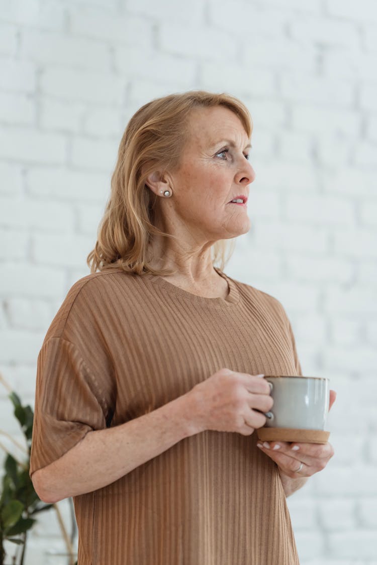 Dreamy Senior Woman Drinking Coffee And Looking Away At Home