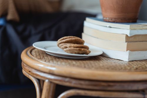 Free Ceramic plate with delicious homemade biscuits served on round wooden table near clay pot placed on stack of books Stock Photo