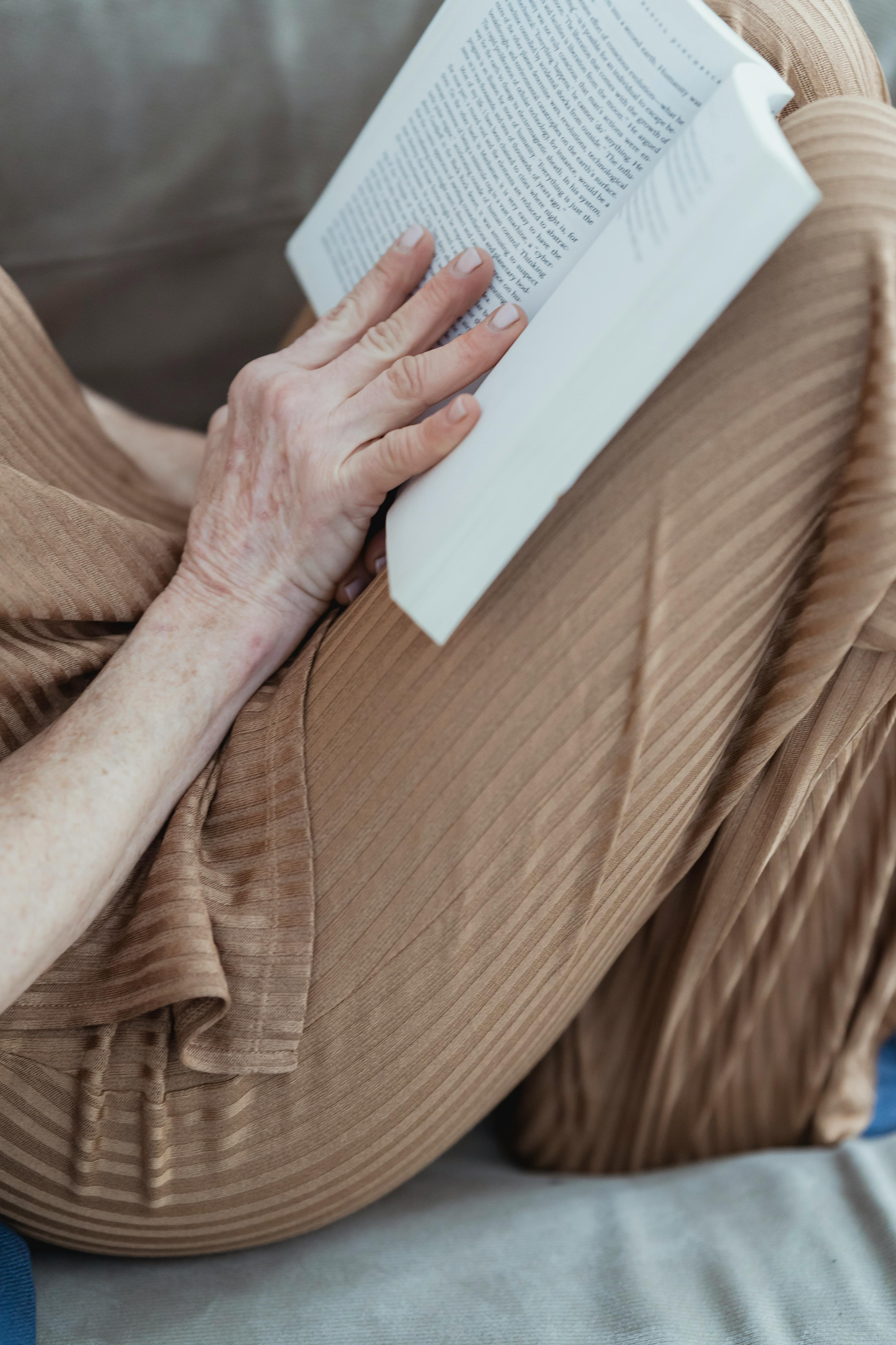 crop unrecognizable woman reading novel on couch during weekend at home