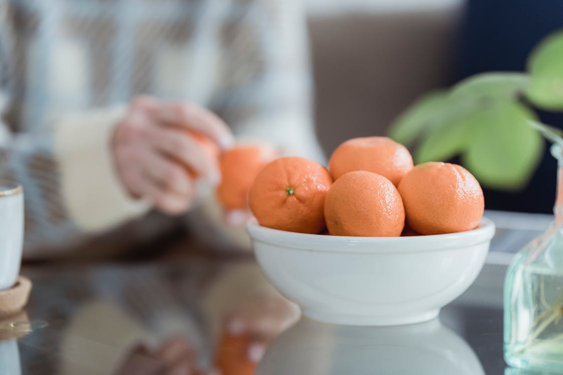 Bowl with fresh tangerines served on table near crop unrecognizable woman