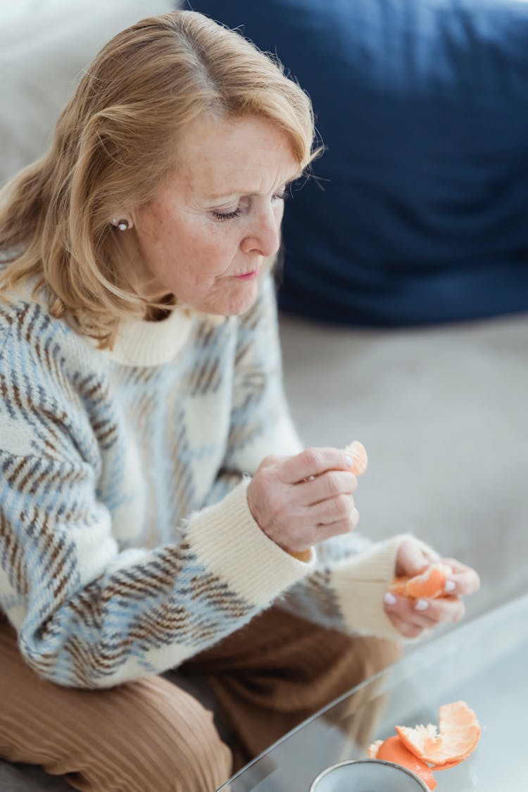 Calm Mature Woman Eating Mandarin During Weekend At Home