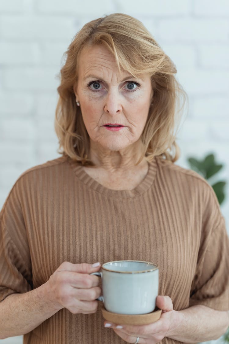 Serious Elderly Woman With Cup Of Coffee In Hand Looking At Camera