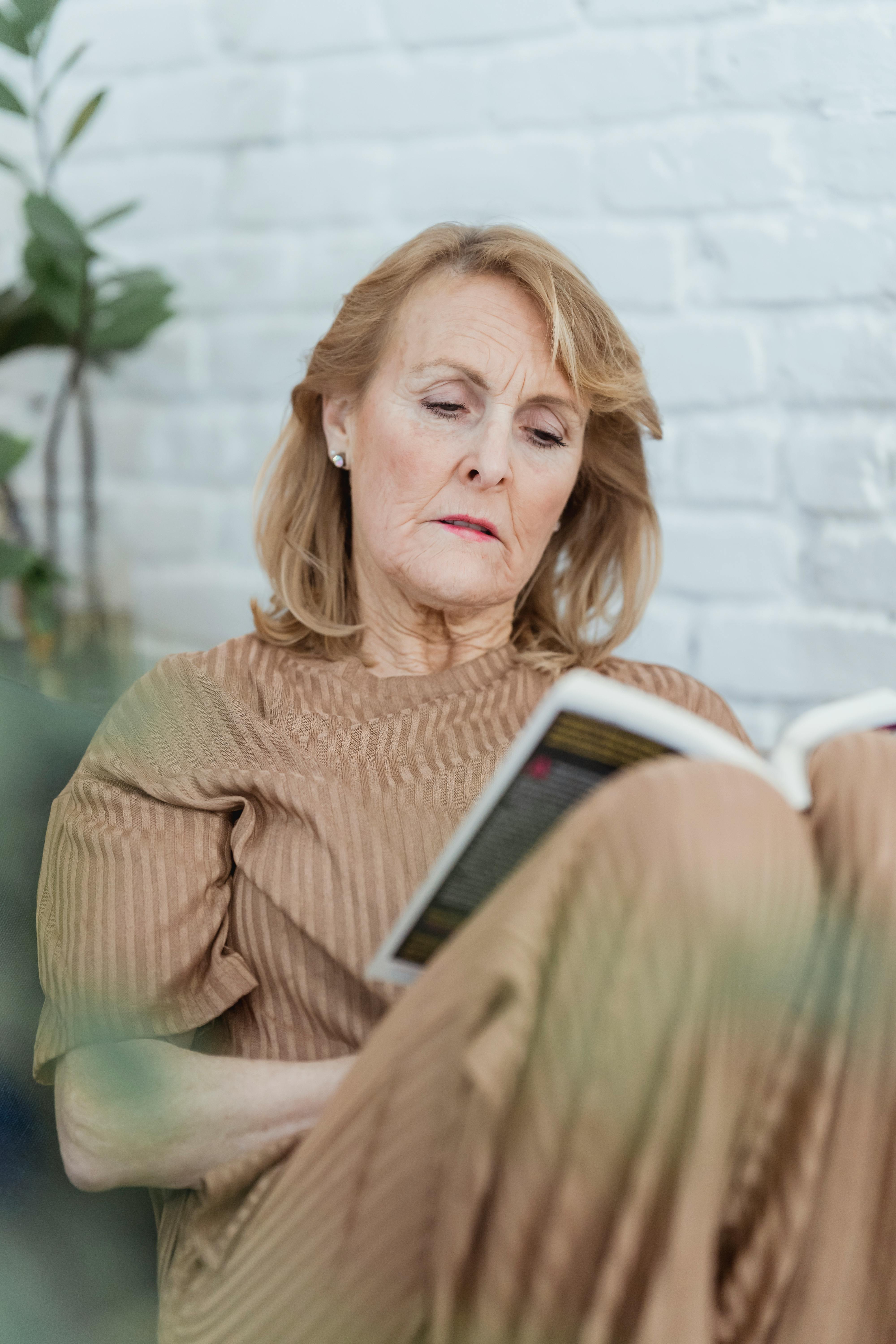 concentrated elderly woman reading interesting novel at home