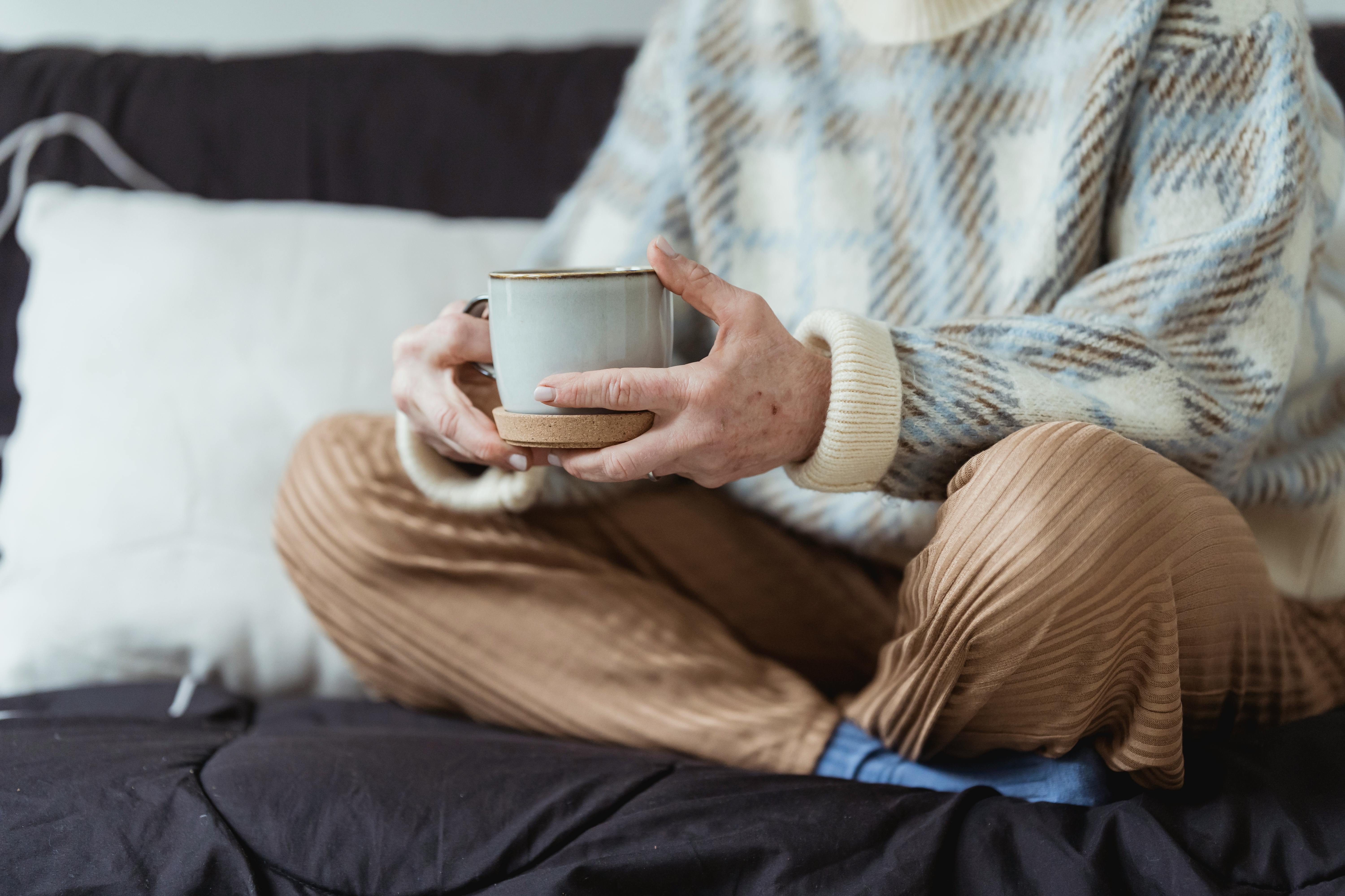 crop faceless woman resting on bed and drinking coffee