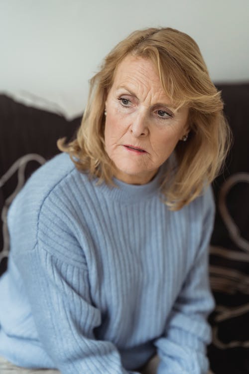 Serious mature woman sitting on comfy couch and looking away