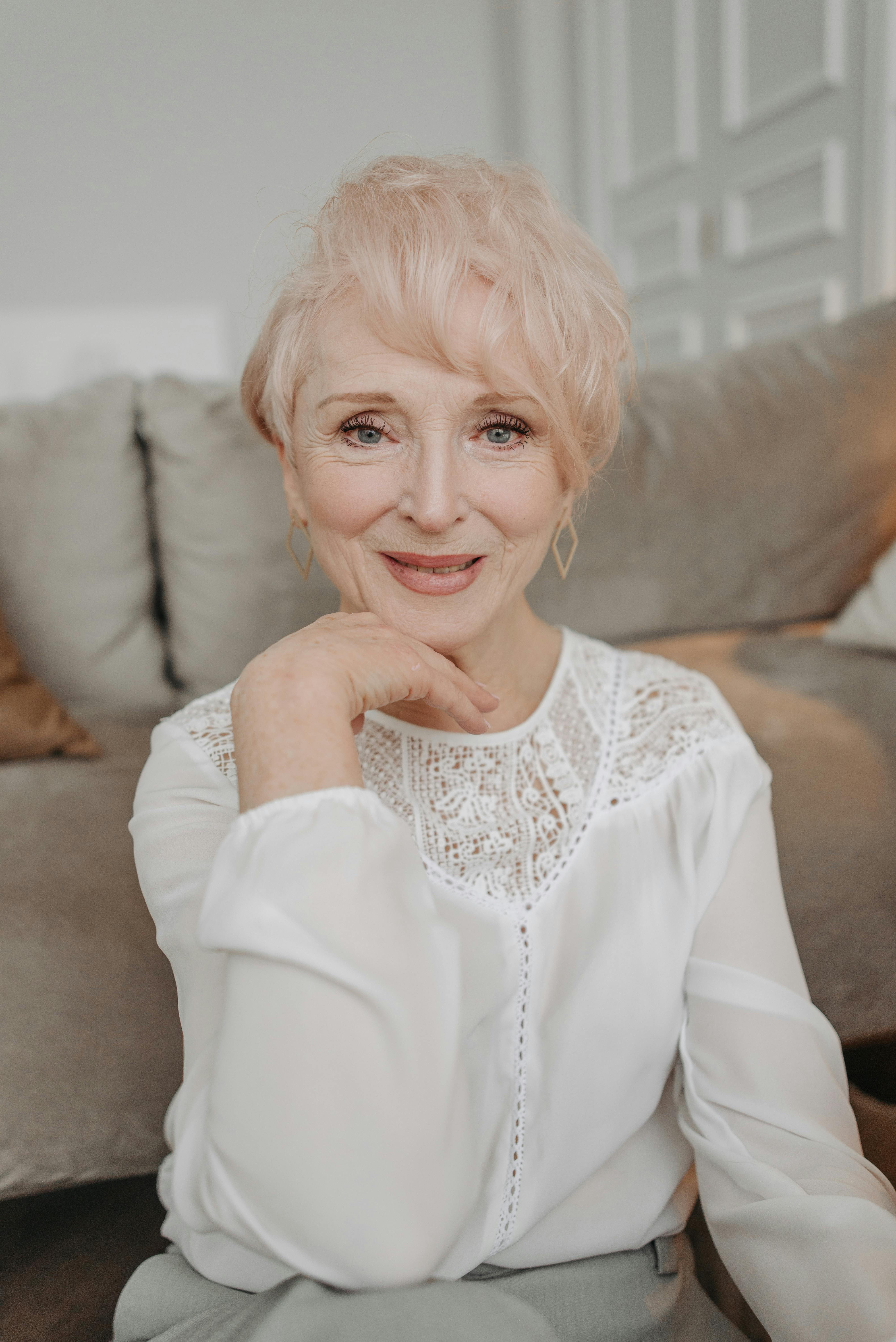 A graceful senior woman with short hair smiling in a cozy indoor environment.