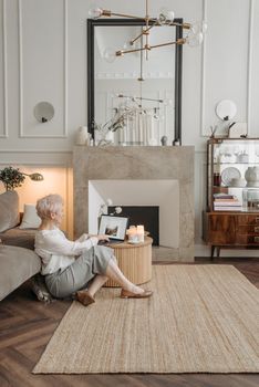 Elderly woman with short hair working remotely on a laptop in a stylish and cozy home setting.