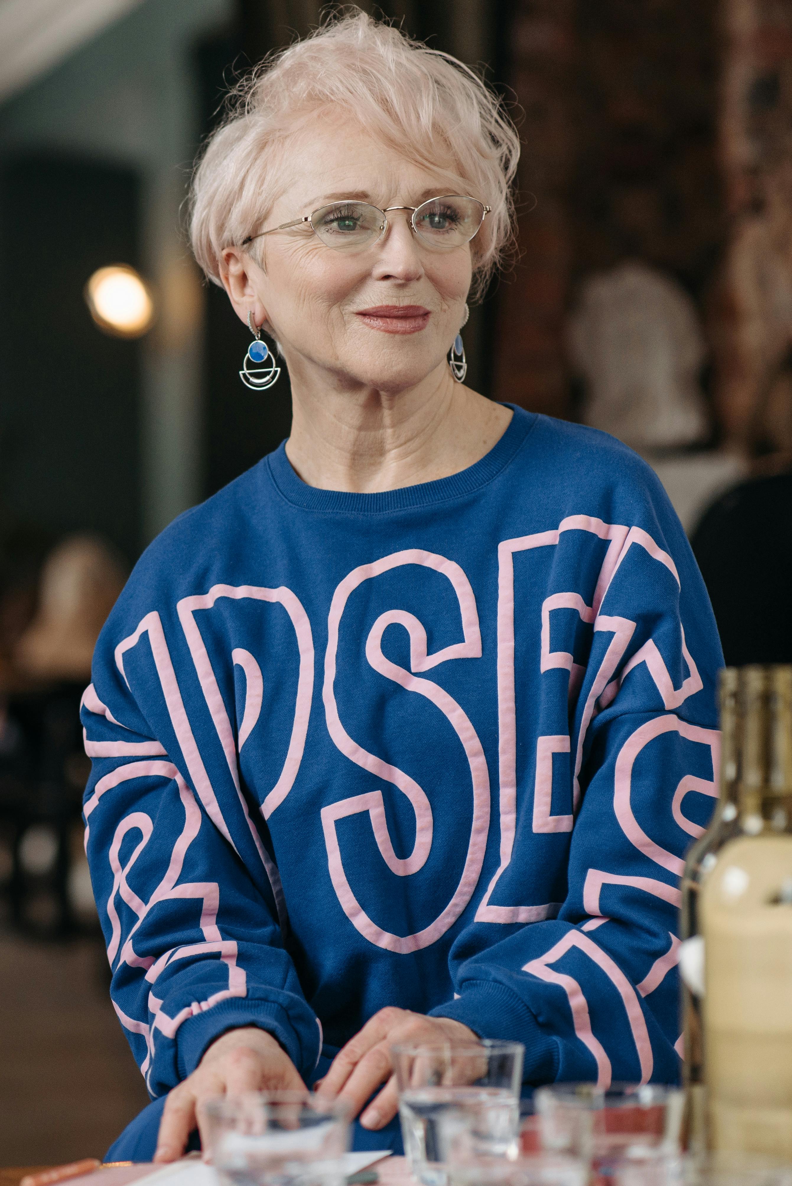 Stylish elderly woman wearing a blue sweater with glasses, captured indoors.