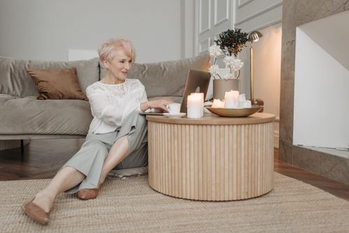 Free Elegant senior woman working on a laptop in a stylish living room setting, surrounded by candles. Stock Photo