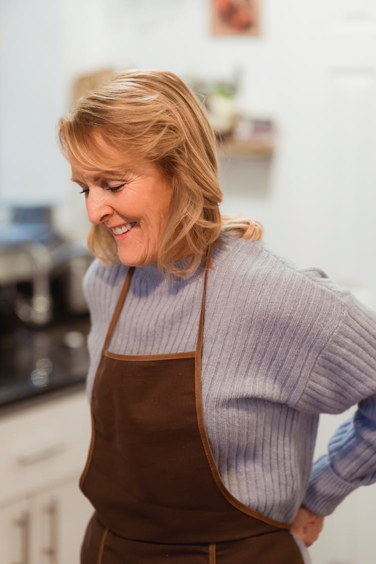 Mature Female In Apron In Kitchen Near Counter