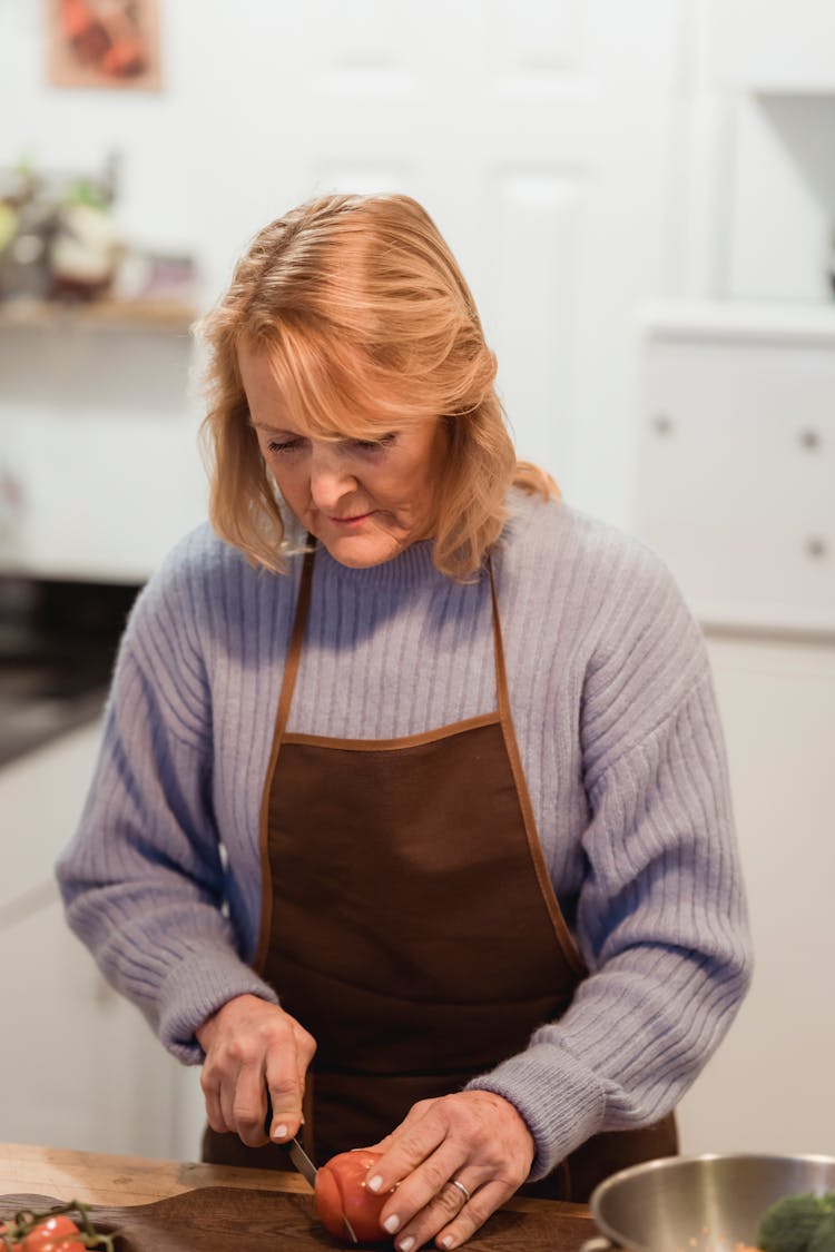 Mature Woman Cutting Ingredient On Kitchen Table With Cutting Board