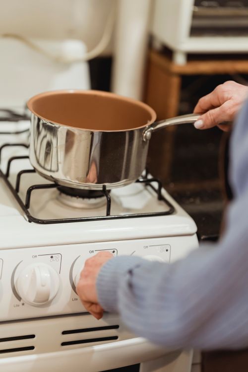 Free Crop anonymous female cook in blue wear placing saucepan on gas stove in light kitchen Stock Photo