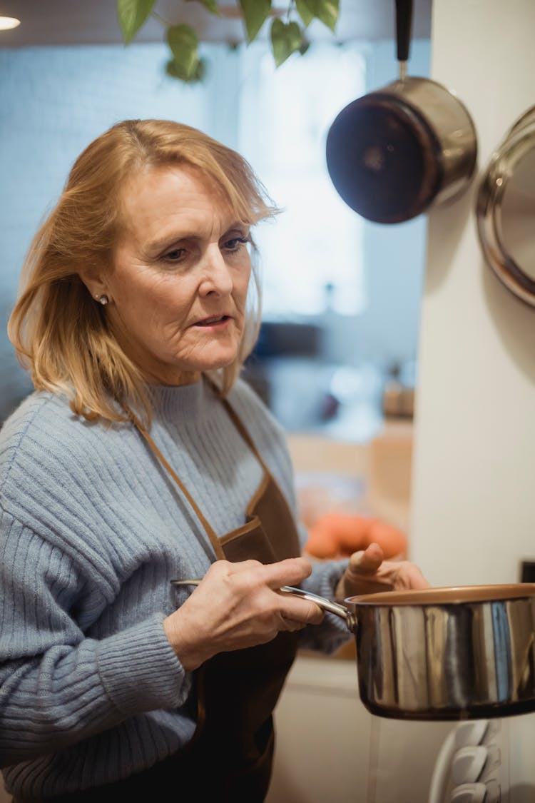 Mature Housewife With Saucepan Standing Near Stove In Kitchen