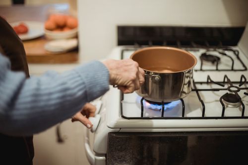 Free Crop anonymous female chef placing saucepan with clean water on burning gad stove while cooking in kitchen Stock Photo