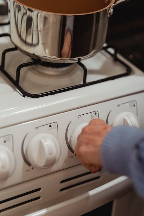 Crop unrecognizable female cook switching gas stove with saucepan while cooking in kitchen