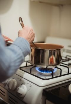 Crop anonymous female cook in blue sweater stirring hot dish in saucepan placed on burning stove in kitchen