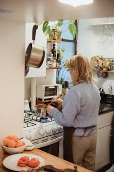 Back view unrecognizable female in apron stirring boiling food in saucepan placed on burning stove while cooking in modern kitchen