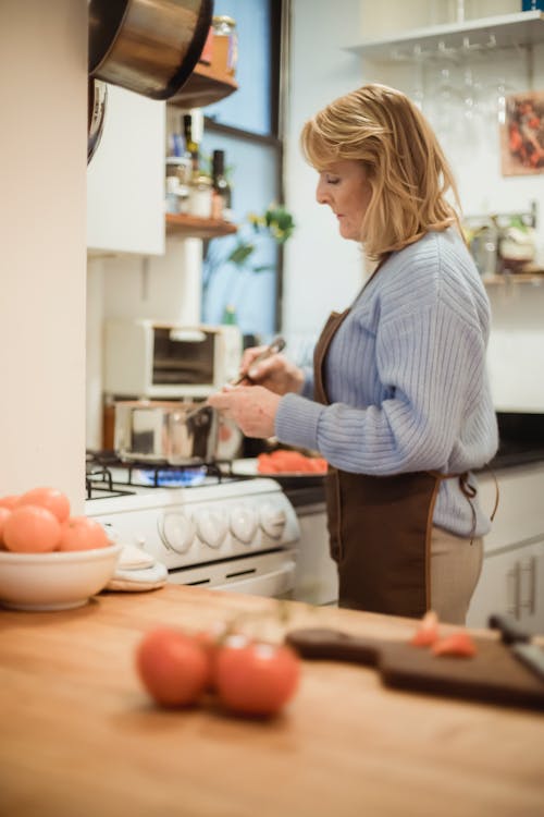 Free Focused mature woman cooking and standing near stove with saucepan Stock Photo