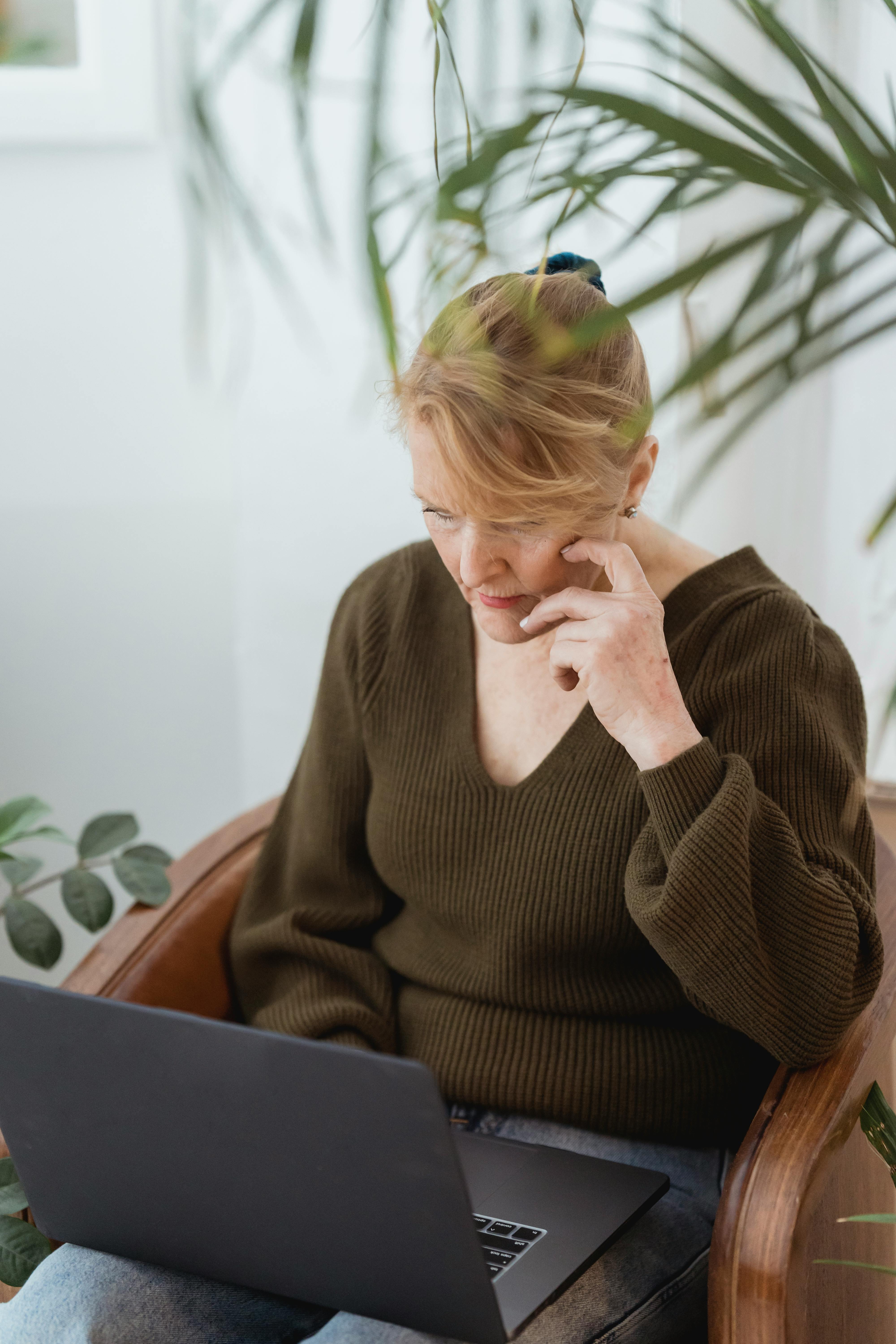 focused mature woman working on laptop on armchair