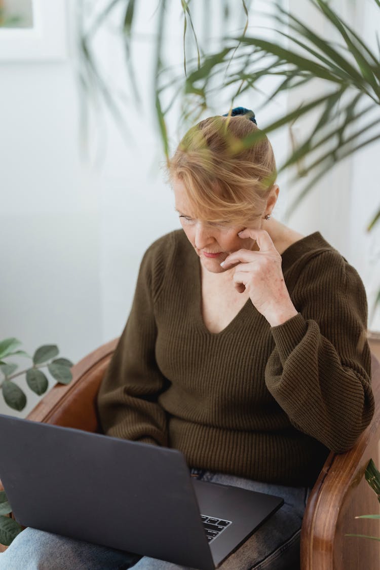 Focused Mature Woman Working On Laptop On Armchair