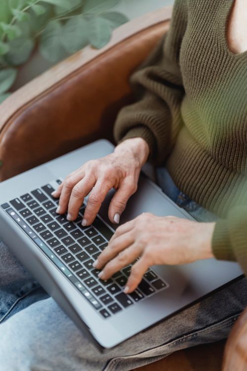 Free Crop unrecognizable female in casual clothes working on modern netbook keyboard while sitting on cozy armchair Stock Photo