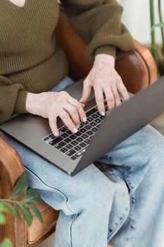 Crop unrecognizable female in casual clothes working on contemporary netbook and sitting on comfy armchair in light room