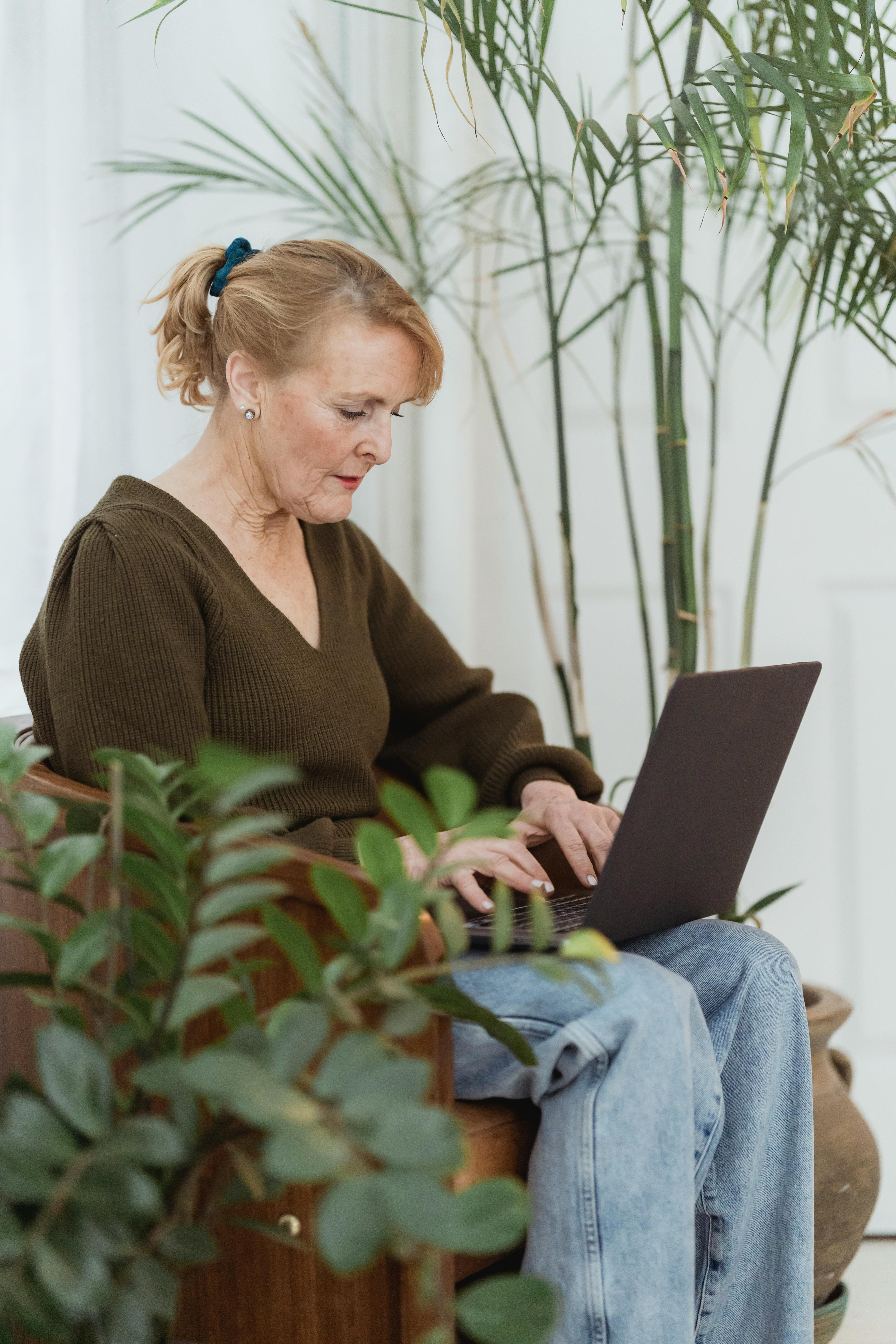 thoughtful mature woman working on laptop on armchair