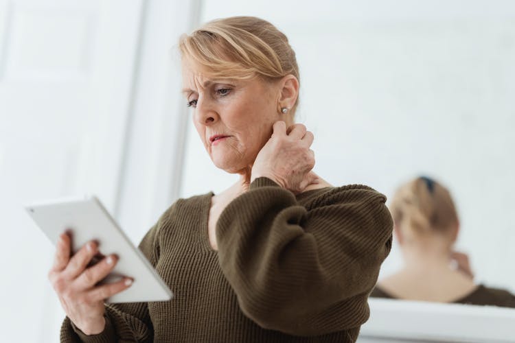 Concerned Mature Woman Using Tablet Against Mirror