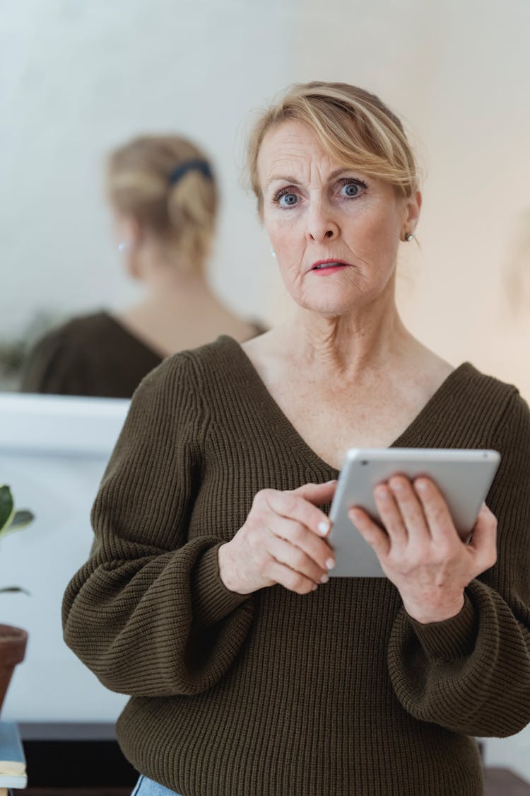 Thoughtful Mature Woman With Tablet Standing In Light Room