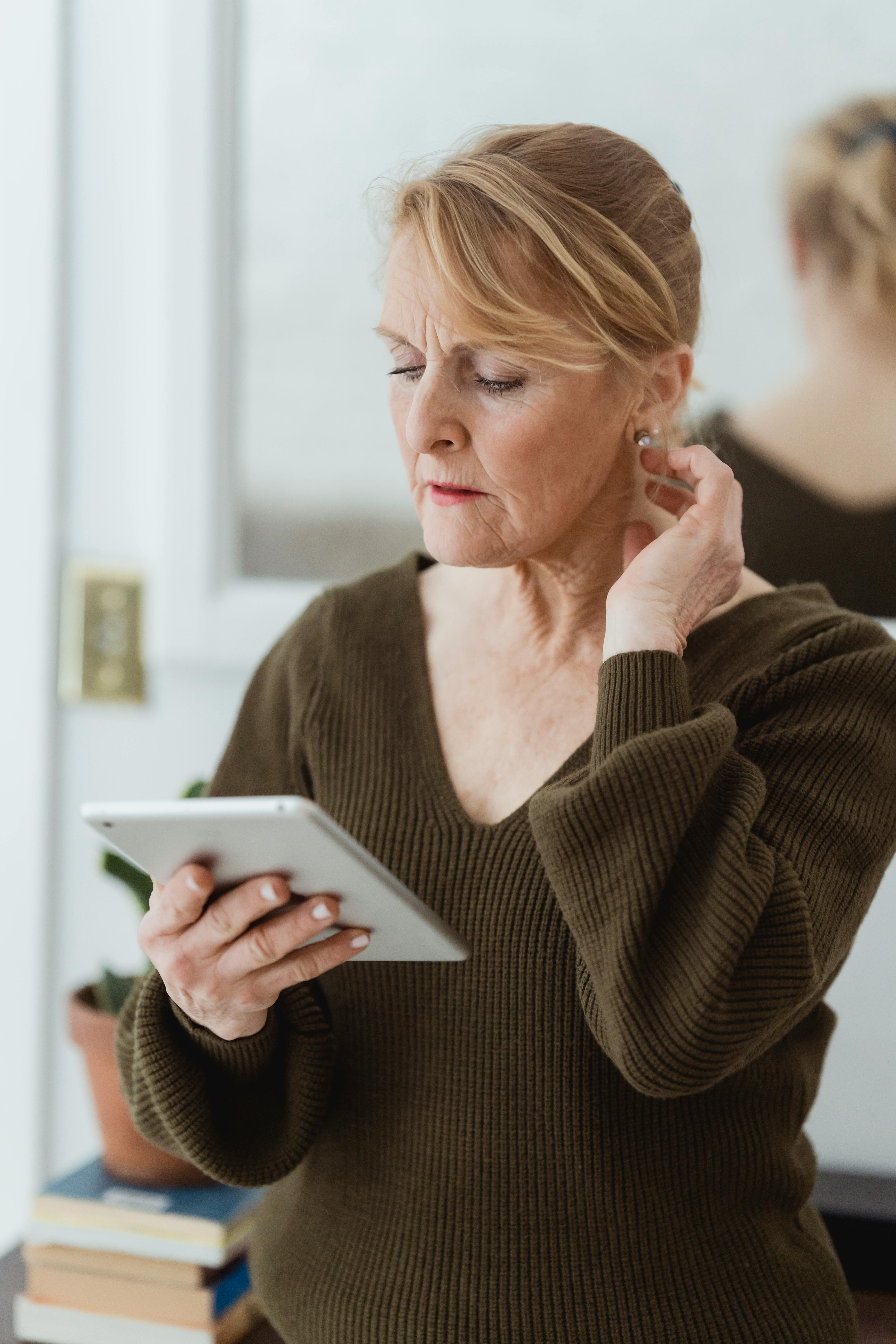 thoughtful mature woman using tablet and touching neck