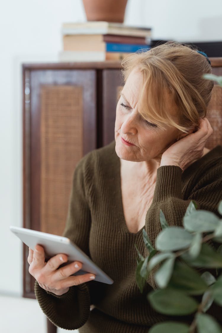 Pensive Mature Woman Using Modern Tablet In Light Room