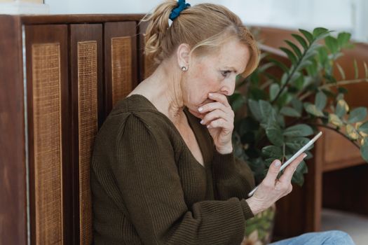 Amazed senior woman with smartphone in house room