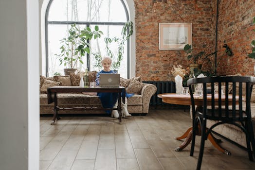 Elegant home office with elderly woman working on a laptop, surrounded by stylish interior design.
