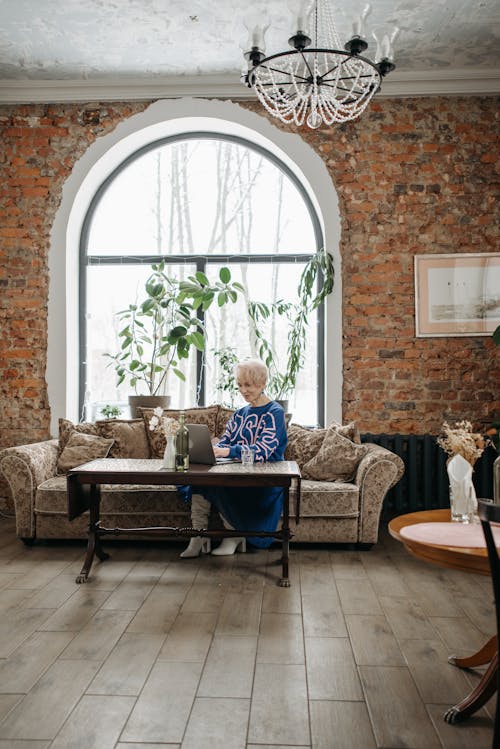 A Woman in Blue Long Sleeves Dress Sitting in a Couch while Typing on a Laptop