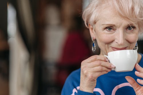 Woman in Blue Long Sleeve Shirt Drinking from White Ceramic Cup