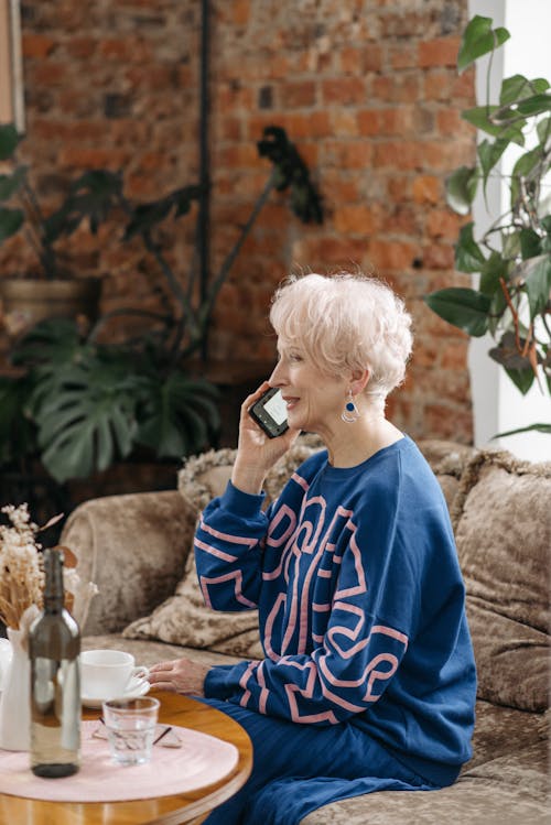 Elderly Woman in Blue Clothes Sitting on Couch Talking on Phone