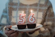 Crop anonymous middle aged female with flaming decorative number candles on tasty chocolate desserts on birthday